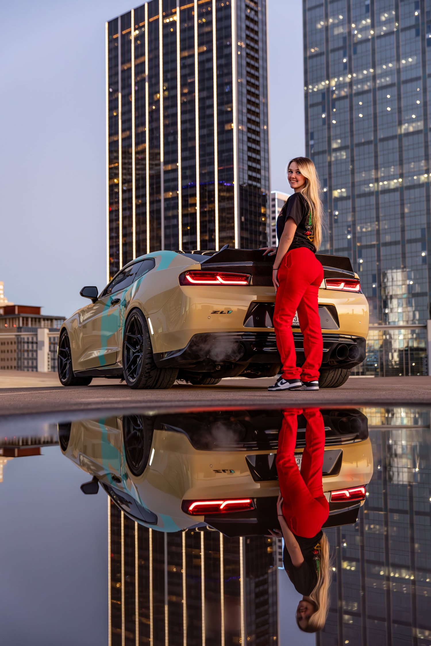Alexxis Pittman standing on her Camaro ZL1 with the Dallas skyline reflected below